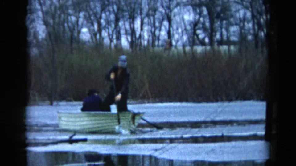 A Wauconda, Illinois rowboat scene from 1961 shows a standing man using an oar near thin ice as another person sits low in the boat.