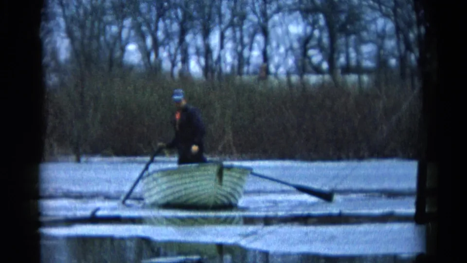 The man shifts upward from the rowboat seat, holding an oar as the boat rests on calm water in Wauconda, Illinois.