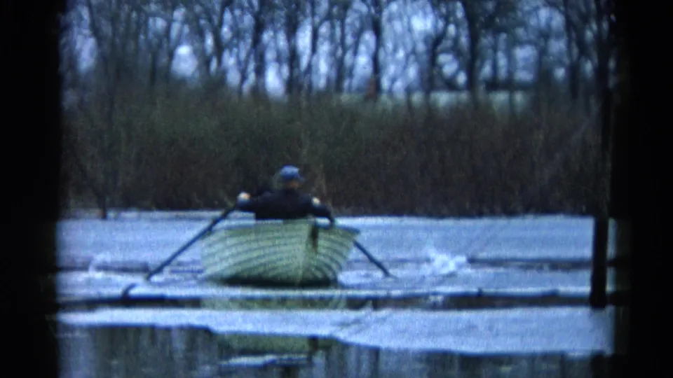Mid-century 8mm frame of an adult rowing a small wooden boat through broken ice on a winter lake in Wauconda, Illinois.