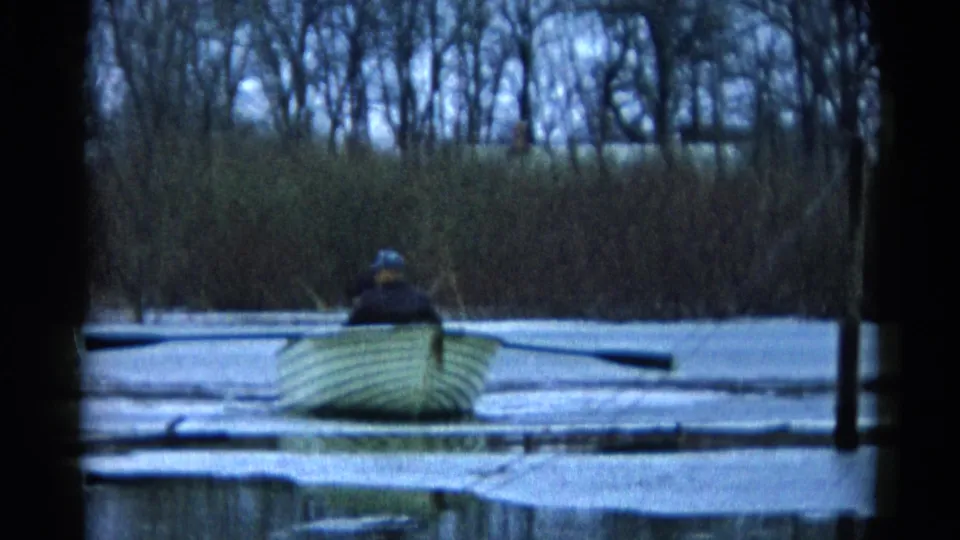 A lone adult rower continues across a partially frozen Wauconda lake, framed by reeds and bare winter trees.