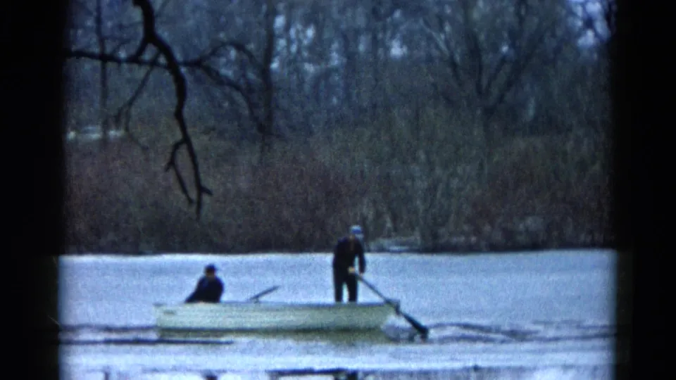 Two people ride in a small rowboat on a calm Wauconda, Illinois lake in 1961, with bare trees and reeds along the far shore.