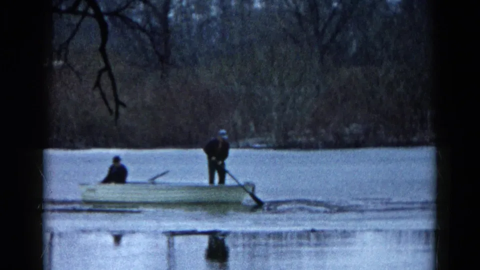 8mm home-movie frame from Wauconda, Illinois showing a small boat cutting through ice with one person standing and one seated.