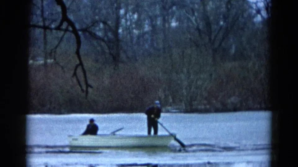 Wauconda, Illinois 1961 home-movie frame showing a small boat, two distant figures, broken ice, and winter shoreline trees.