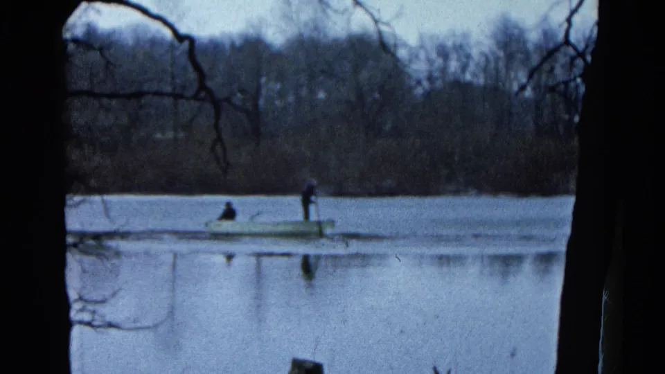 1961 Wauconda, Illinois 8mm frame showing a small boat with two distant people on calm water, bordered by dark tree silhouettes.