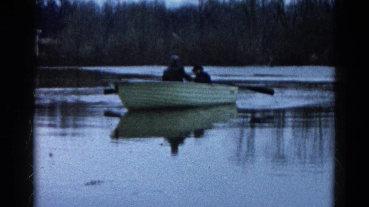 1961 Wauconda, Illinois home-movie frame showing two distant people in a small rowboat on still water under muted light.