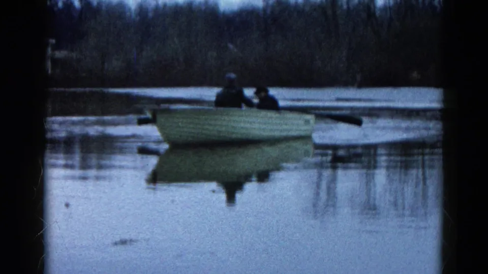1961 Wauconda, Illinois home-movie frame showing two distant people in a small rowboat on still water under muted light.