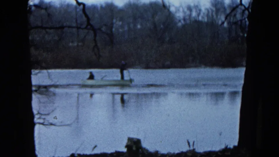 1961 Wauconda, Illinois frame showing a rowboat near the far shore, with two distant figures and reflections on the lake.