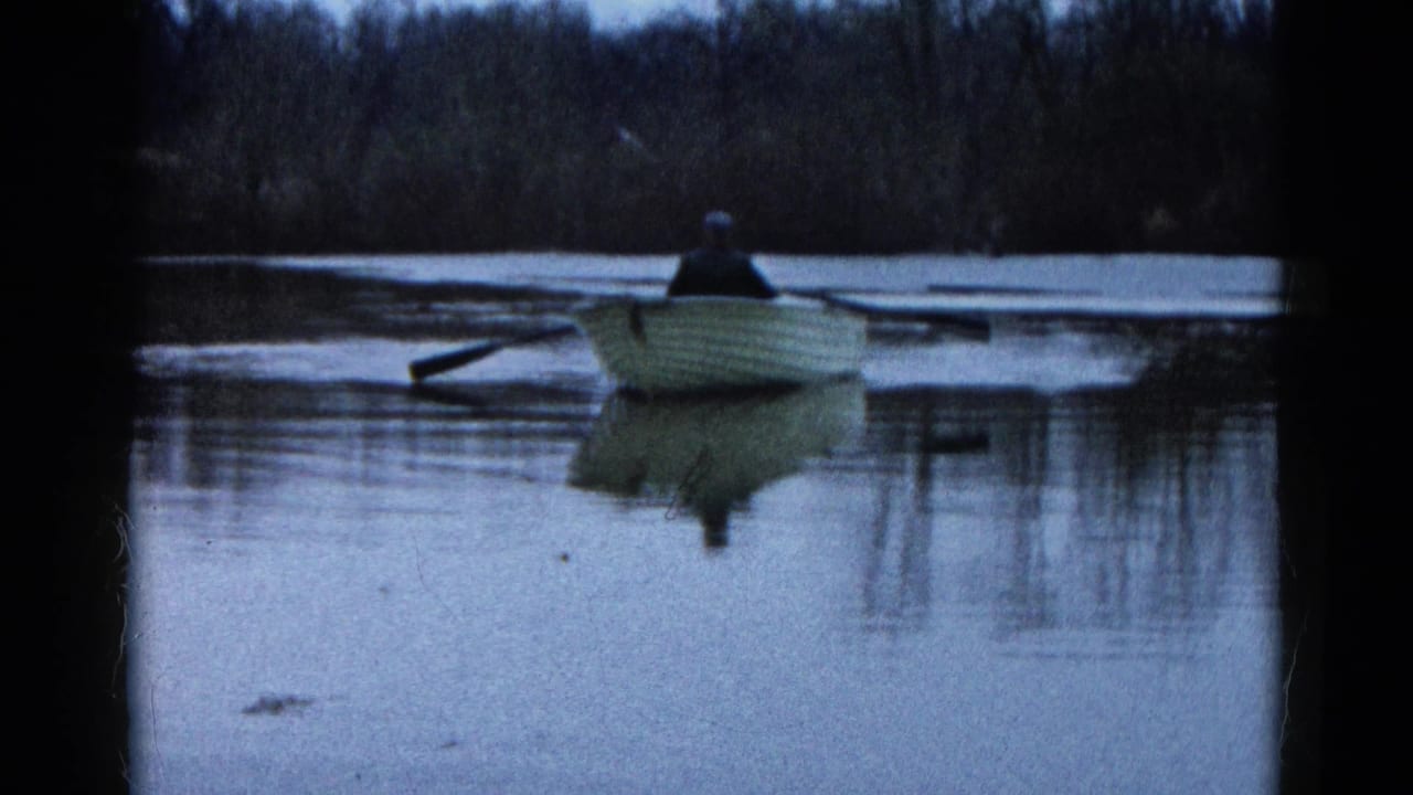 A lone person rows a small pale boat across a calm lake at dusk.