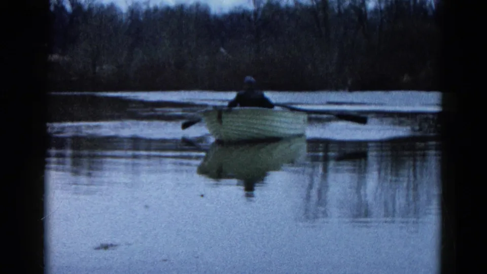 1961 Wauconda lake view with a lone rower using extended oars in a small boat, reflected in the dim water.