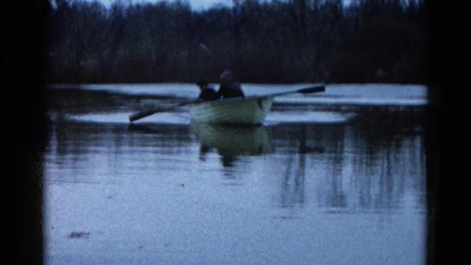 1961 Wauconda, Illinois lake scene with two people in a small rowboat, its oars and reflection visible on blue-toned water.
