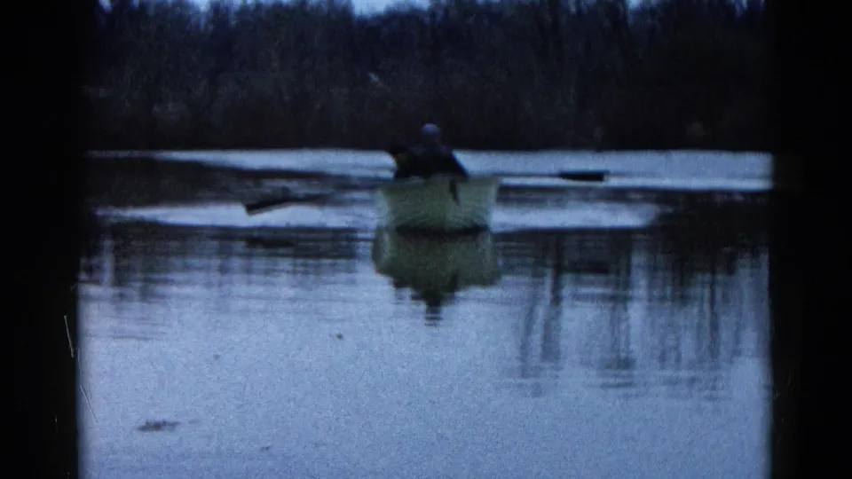 1961 Wauconda, Illinois 8mm footage frame showing the rowboat from behind as two people continue across the lake.