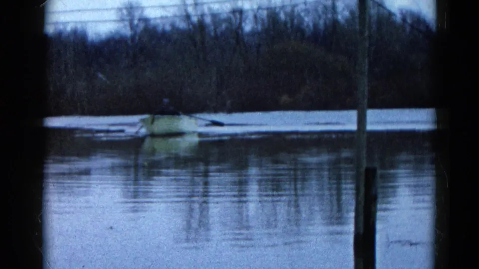 The 1961 Wauconda home-movie frame shows the yellow rowboat near a distant shore, partly obscured by film-frame edges and soft focus.