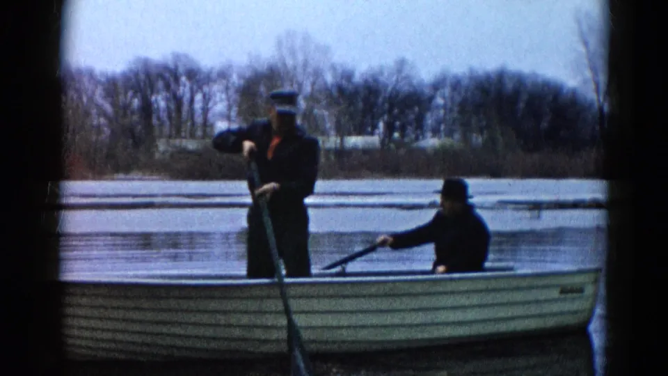 1961 Wauconda, Illinois home-movie still of two men in a rowboat on calm water, framed by dark 8mm film edges.
