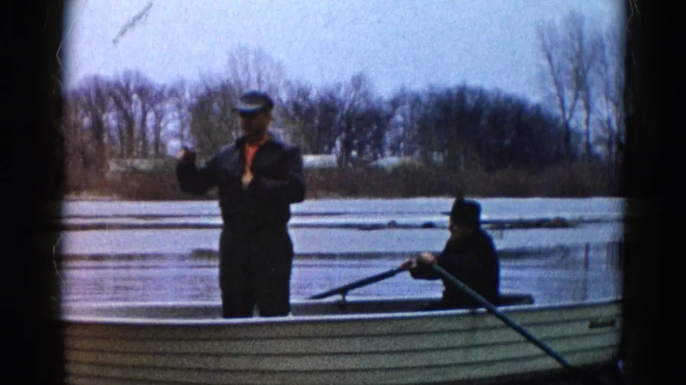 A man in a cap gestures while standing in a canoe on a Wauconda lake, as another man sits nearby with a paddle.
