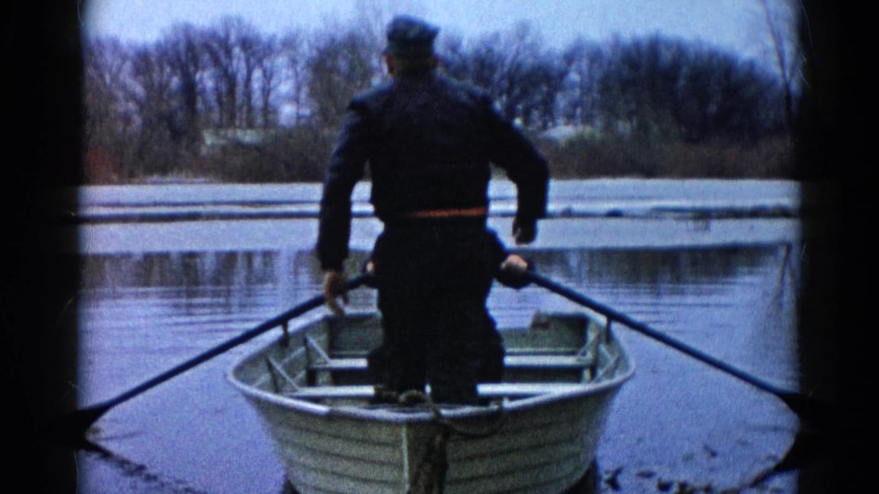 In Wauconda, Illinois, 1961, an adult in dark clothing rows a small aluminum boat across icy water.