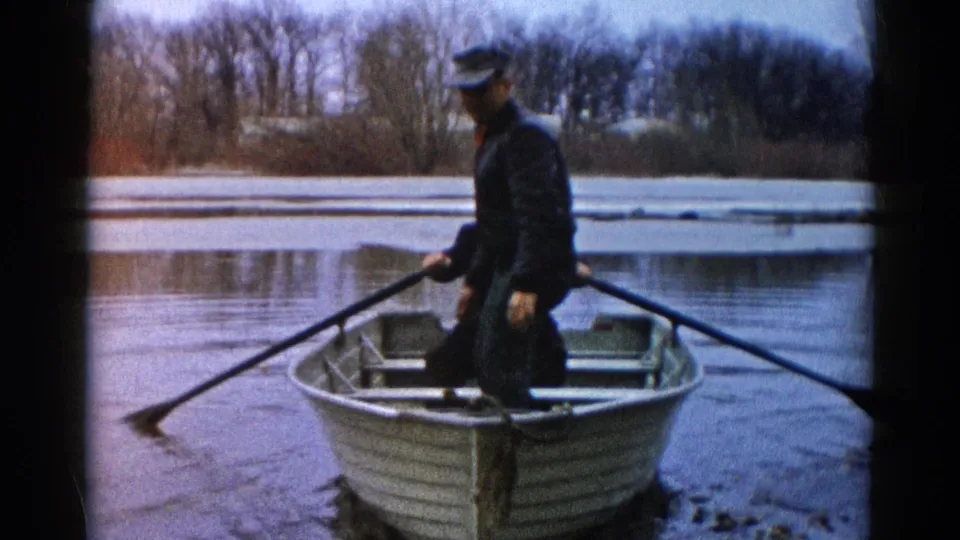 An adult rows a small aluminum boat across a calm, icy river in the supplied Wauconda, Illinois 1961 footage.