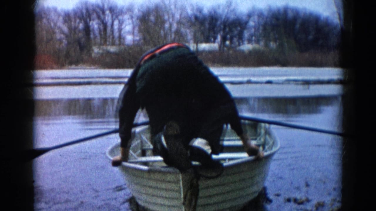 Man bending over a small aluminum rowboat at the edge of a cold lake.