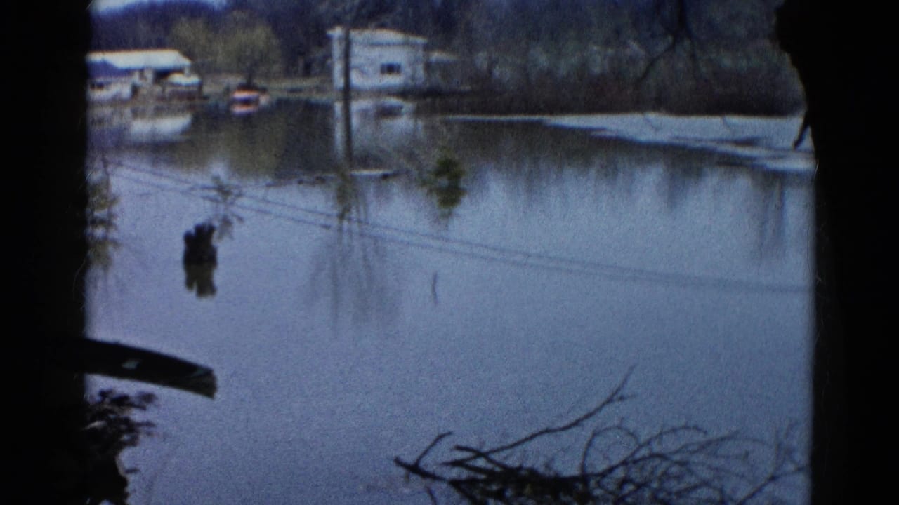 Floodwater surrounds distant houses and trees, with utility lines crossing the frame.
