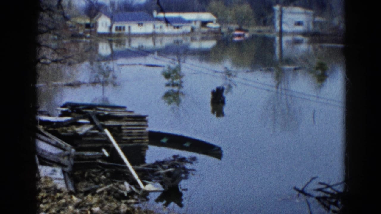 1961 Wauconda, Illinois 8mm frame showing floodwater, shoreline debris, bare trees, and distant houses reflected in still water.