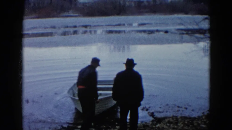 Two men appear to guide or launch a rowboat at the edge of a calm Wauconda lake in 1961 8mm footage.