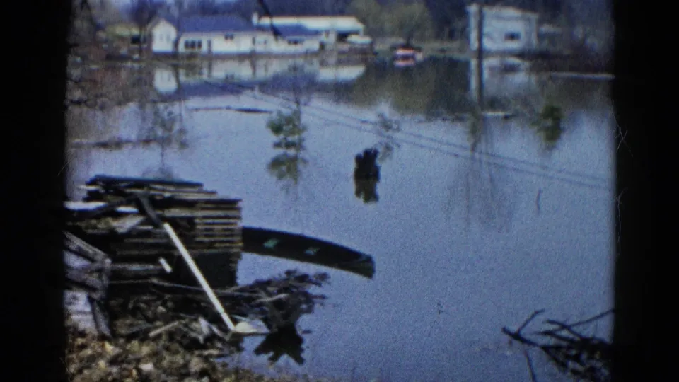 A flooded residential area in Wauconda, Illinois, shows water around houses, shoreline debris, and the edge of a small boat in 1961 footage.