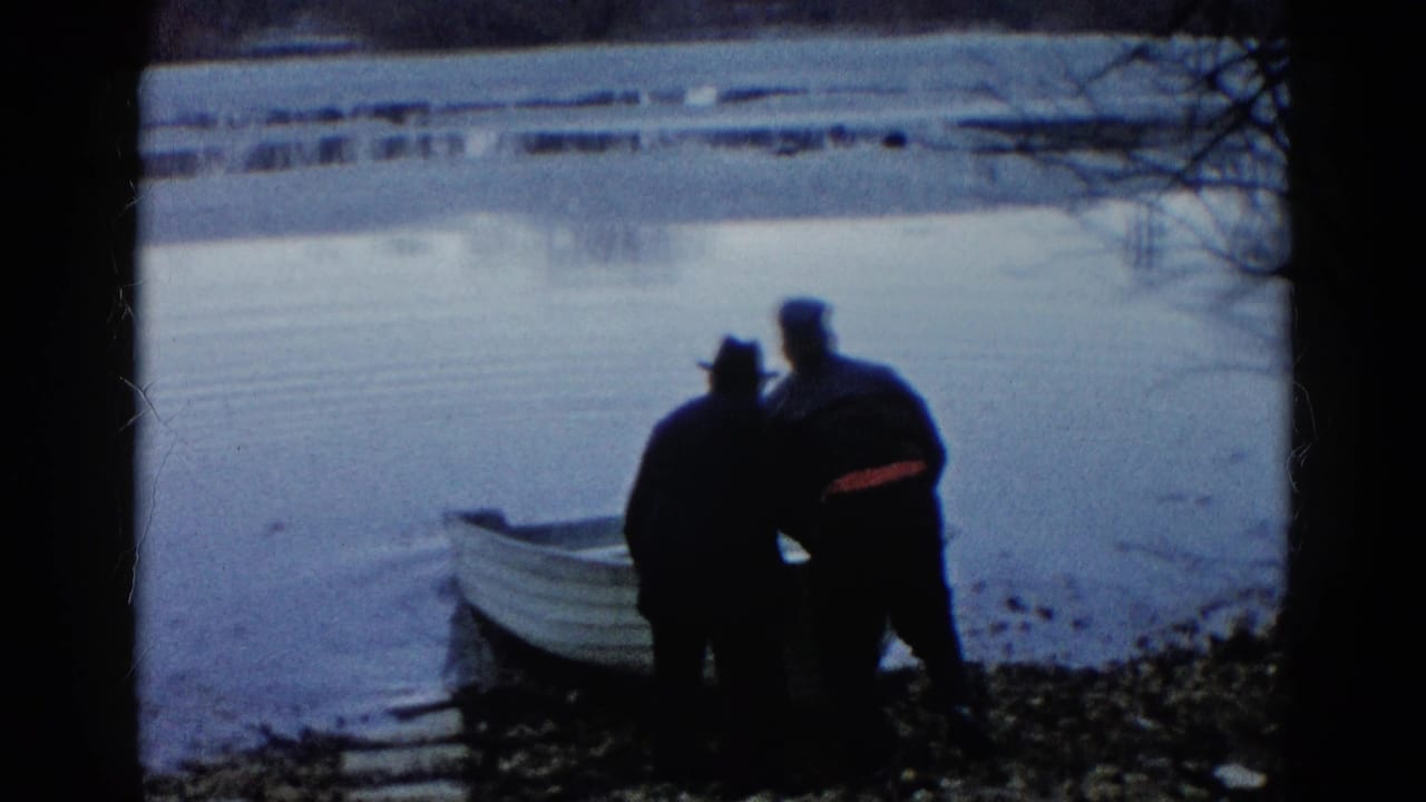 Two men stand beside a small white rowboat at a calm lakeshore.