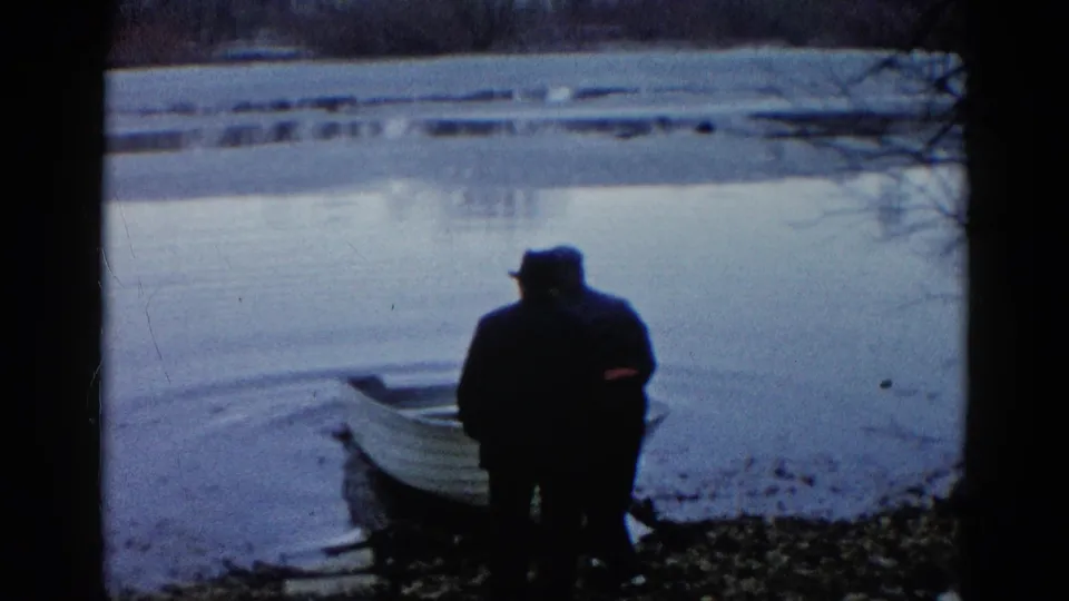 Two older men, seen mostly in silhouette, face a calm lake beside a small white rowboat in 1961 Wauconda footage.