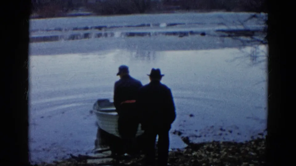 Two men in coats and hats stand at the lakeshore as a small rowboat sits partly in the water in Wauconda, Illinois.
