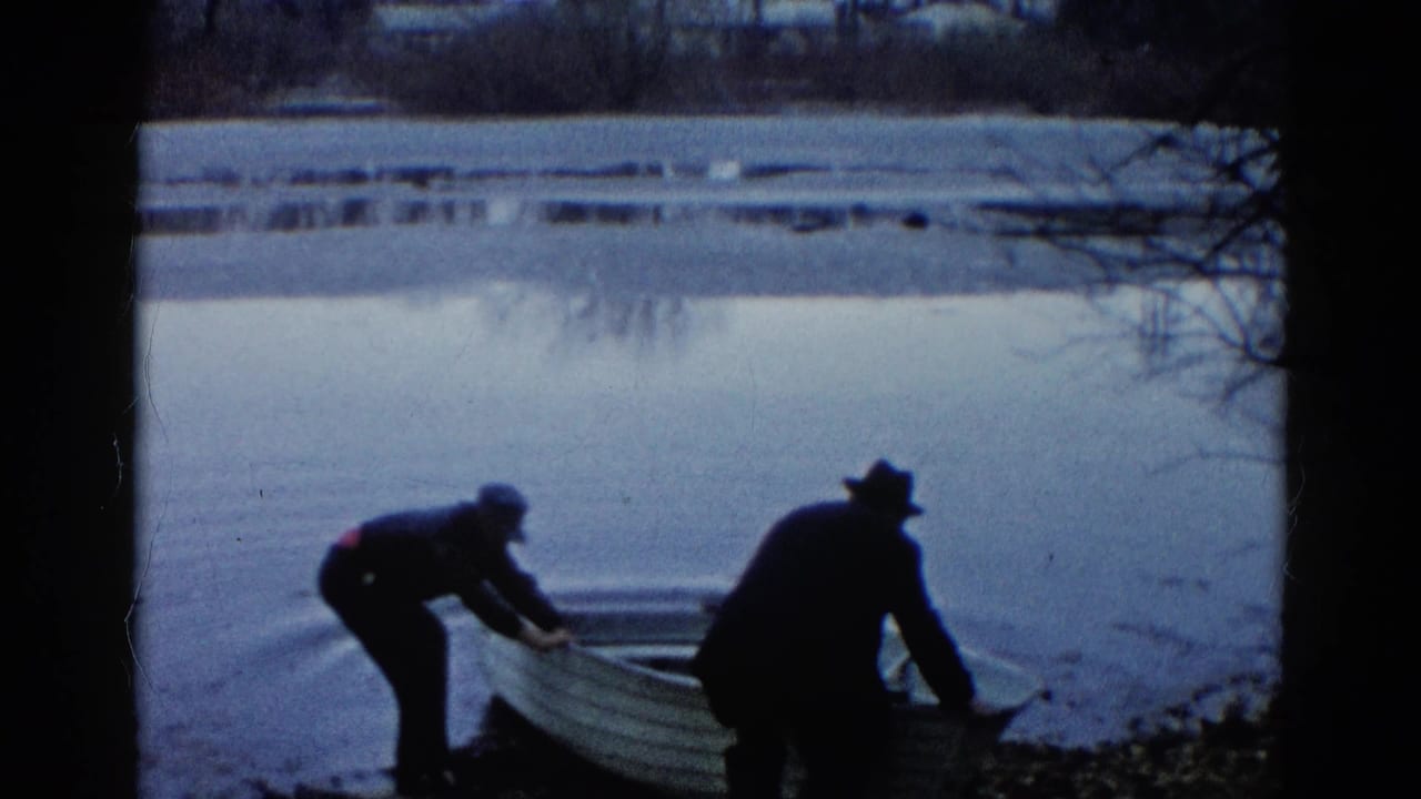 In supported 1961 Wauconda, Illinois footage, two men in hats push a small rowboat into a quiet lake from the shoreline.