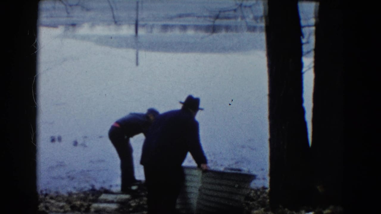 In 1961 Wauconda, Illinois, two adult men appear to prepare a light rowboat at the edge of a calm lake.