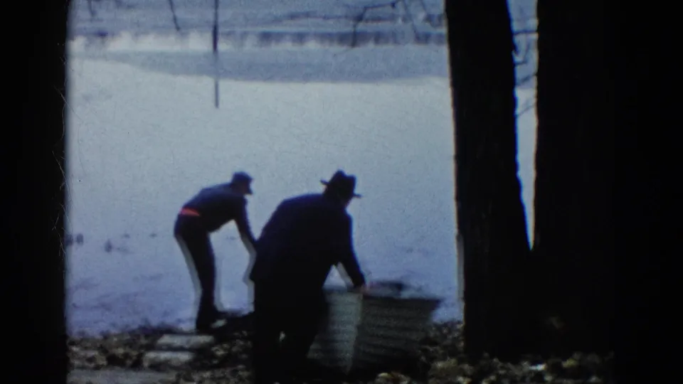 Two men work at the shore in Wauconda, Illinois, with a small rowboat partly angled toward the lake.