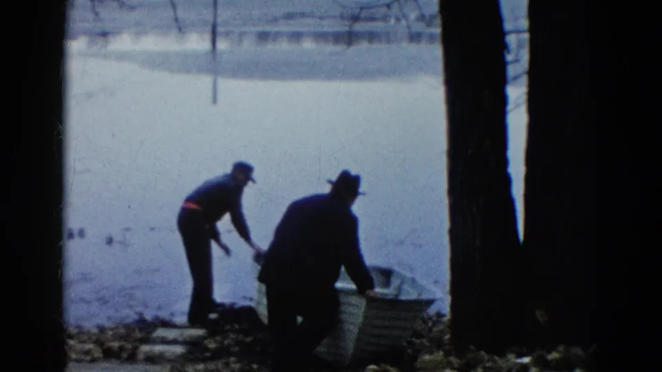 The 8mm frame shows two men guiding a light-colored rowboat at a Wauconda lakeshore in 1961.