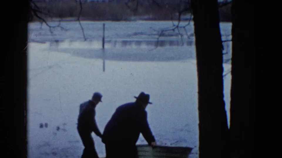 The men begin working at the rowboat on the snowy Wauconda shoreline, bending toward its side in the winter scene.
