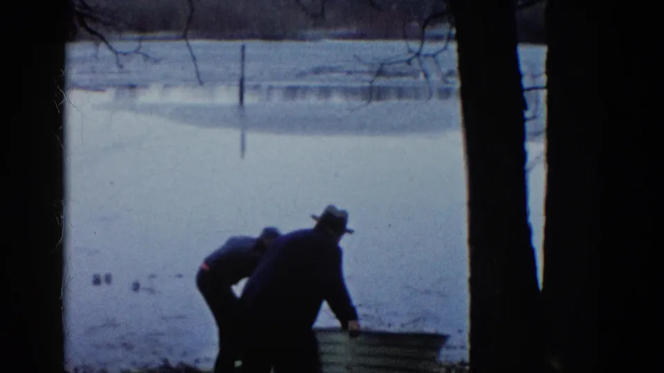 In the final frame, two men lean over the rowboat near the frozen lake, partly silhouetted by dark foreground trees.