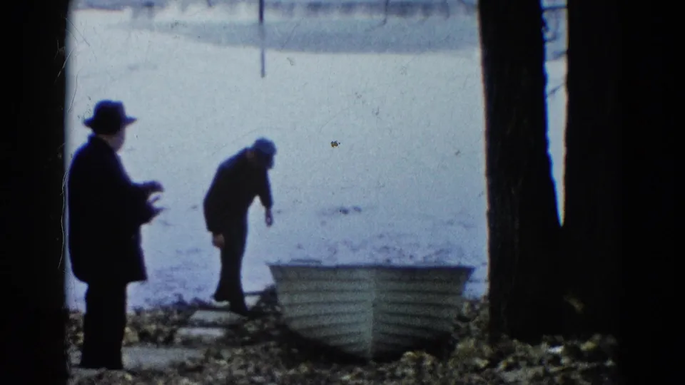 Two men remain beside the small white rowboat on the Wauconda shoreline, with one bending near the boat and one standing back.
