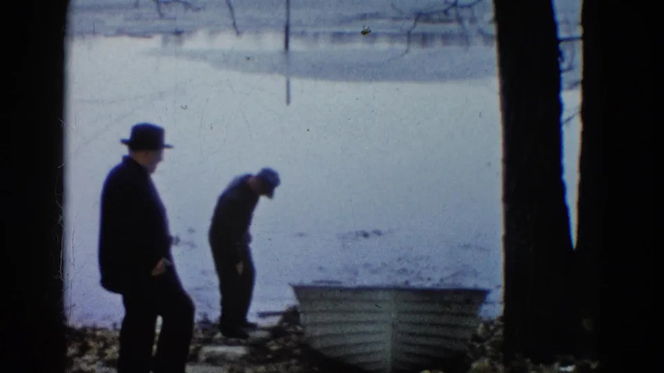 At the end of the 1961 Wauconda clip, two men stand near the rowboat on the shore under cool, overcast light.