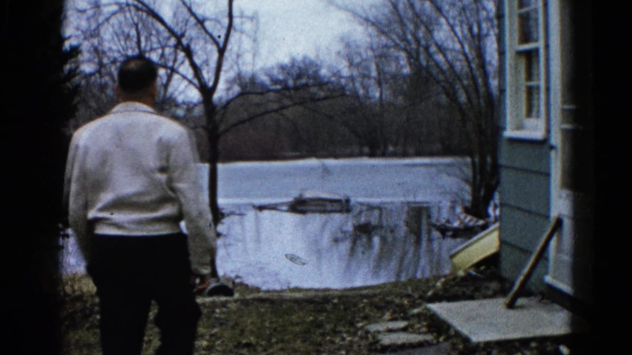 Man seen from behind walking out from a house toward a flooded yard.