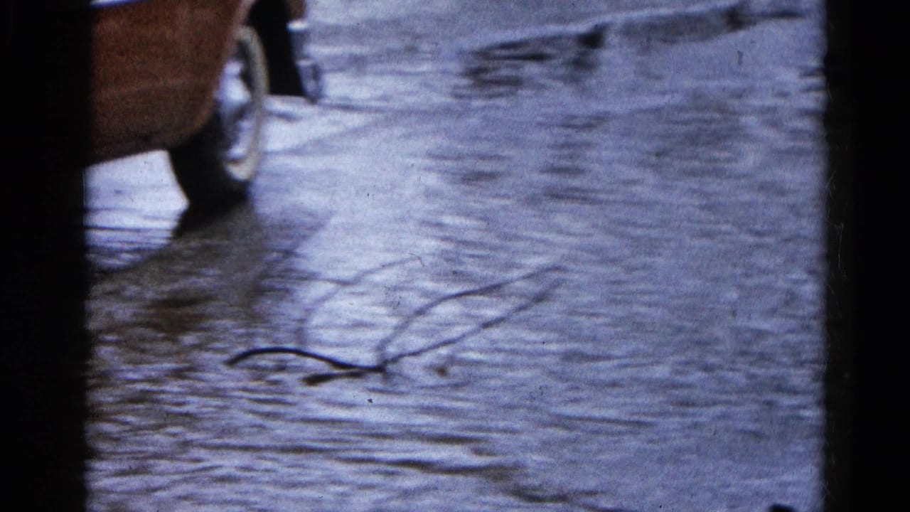 1961 Wauconda, Illinois home-movie frame showing a partial classic car beside floodwater covering the roadway.