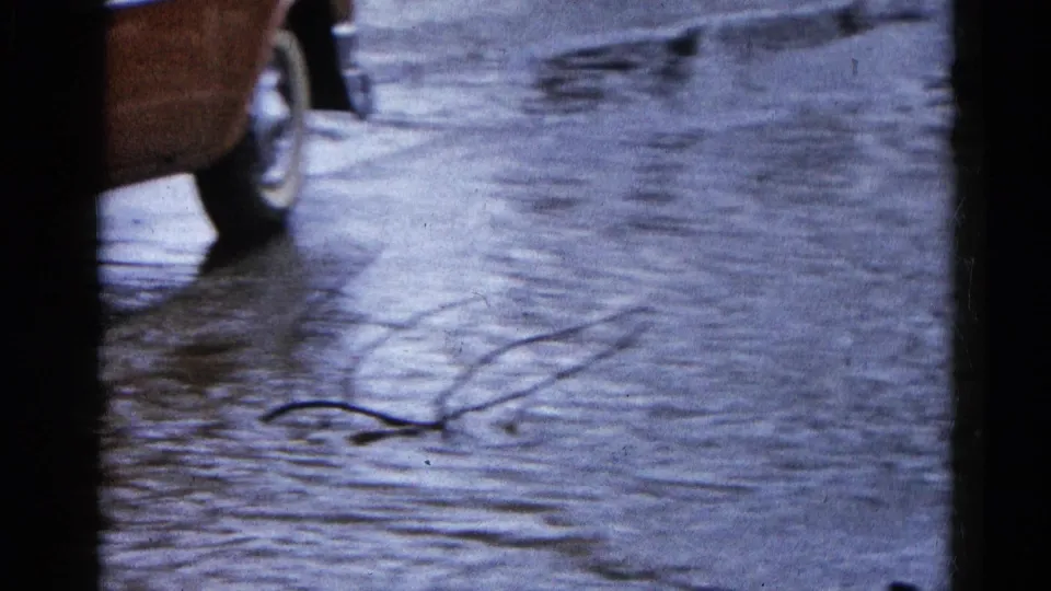 1961 Wauconda, Illinois home-movie frame showing a partial classic car beside floodwater covering the roadway.
