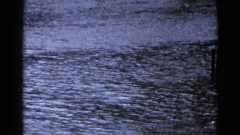 Final 1961 Wauconda frame showing rippling floodwater and a dark vertical trunk or post near the roadway.