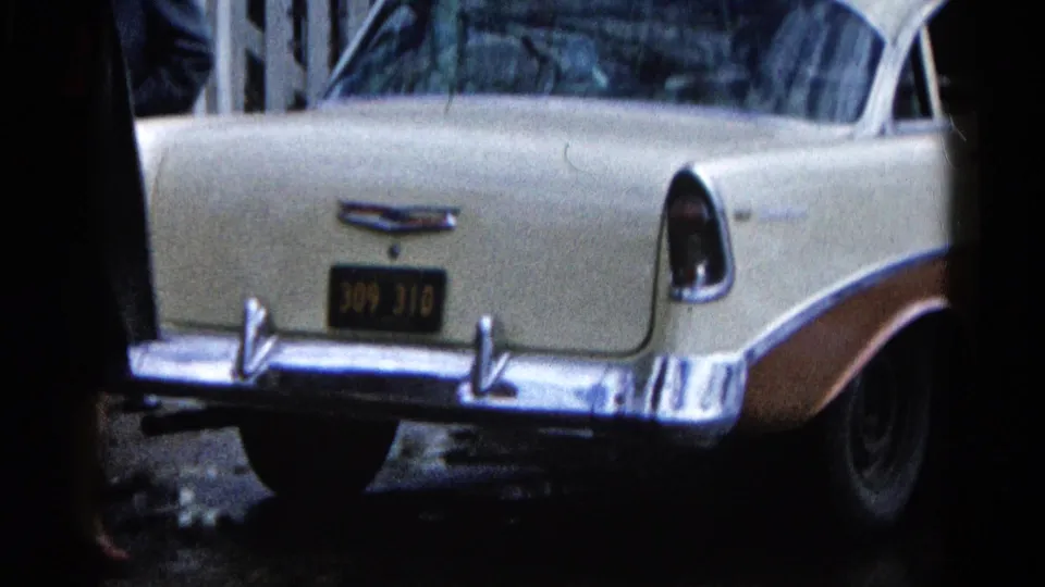Cream-and-brown Chevrolet rear remains parked on the wet Wauconda street, with tail fins, chrome bumper, and plate area visible.