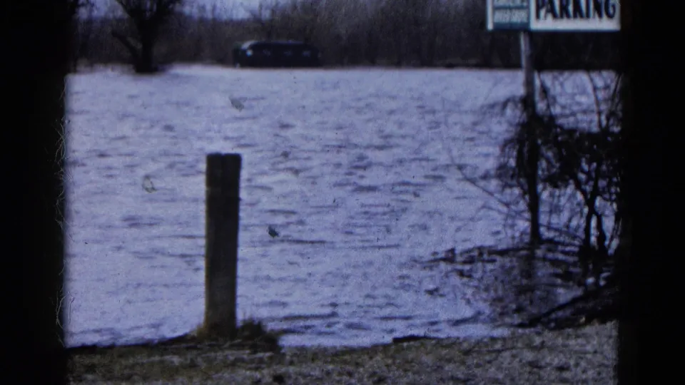 1961 Wauconda, Illinois floodwater covers a parking area around a wooden post, with a dark car partly submerged beyond it.