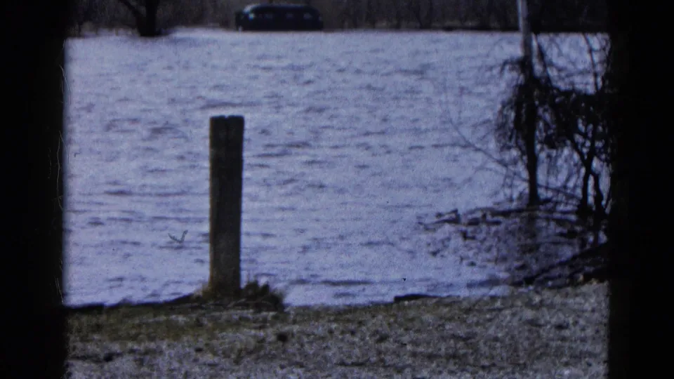The final frame shows Wauconda floodwater moving through a parking area, with a foreground post, brush, and a dark car beyond.