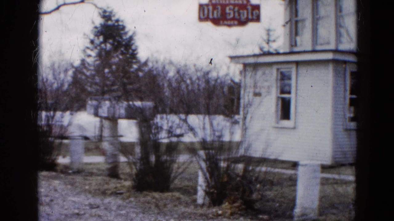 White roadside building with an Old Style sign near bare shrubs and wet ground.