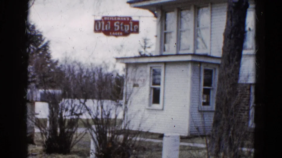 1961 Wauconda, Illinois frame of a white two-story house with Old Style Lager signage, bare winter shrubs, and dark film-edge borders.