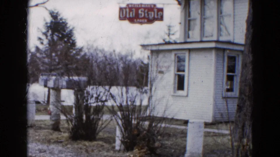 Final 1961 Wauconda, Illinois frame with a white house, visible Old Style Lager sign, leafless shrubs, winter grass, and overcast sky.