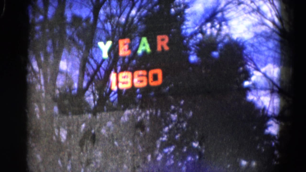Wauconda, Illinois 8mm frame with colored YEAR 1960 lights against bare trees and a dark wooded backdrop.