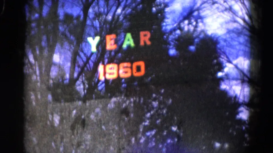 Wauconda, Illinois 8mm frame with colored YEAR 1960 lights against bare trees and a dark wooded backdrop.