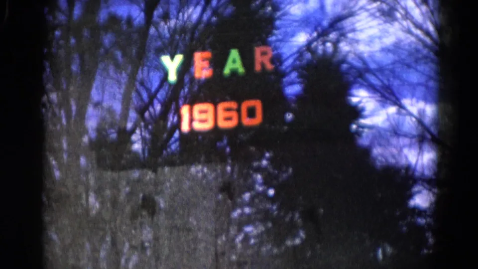 1961 Wauconda 8mm frame showing a reflected YEAR 1960 sign over bare trees against a blue sky.