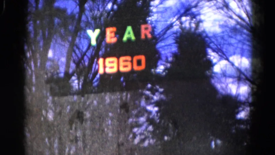 Soft 8mm frame of the YEAR 1960 sign reflection, with bare branches and blue-purple sky tones.